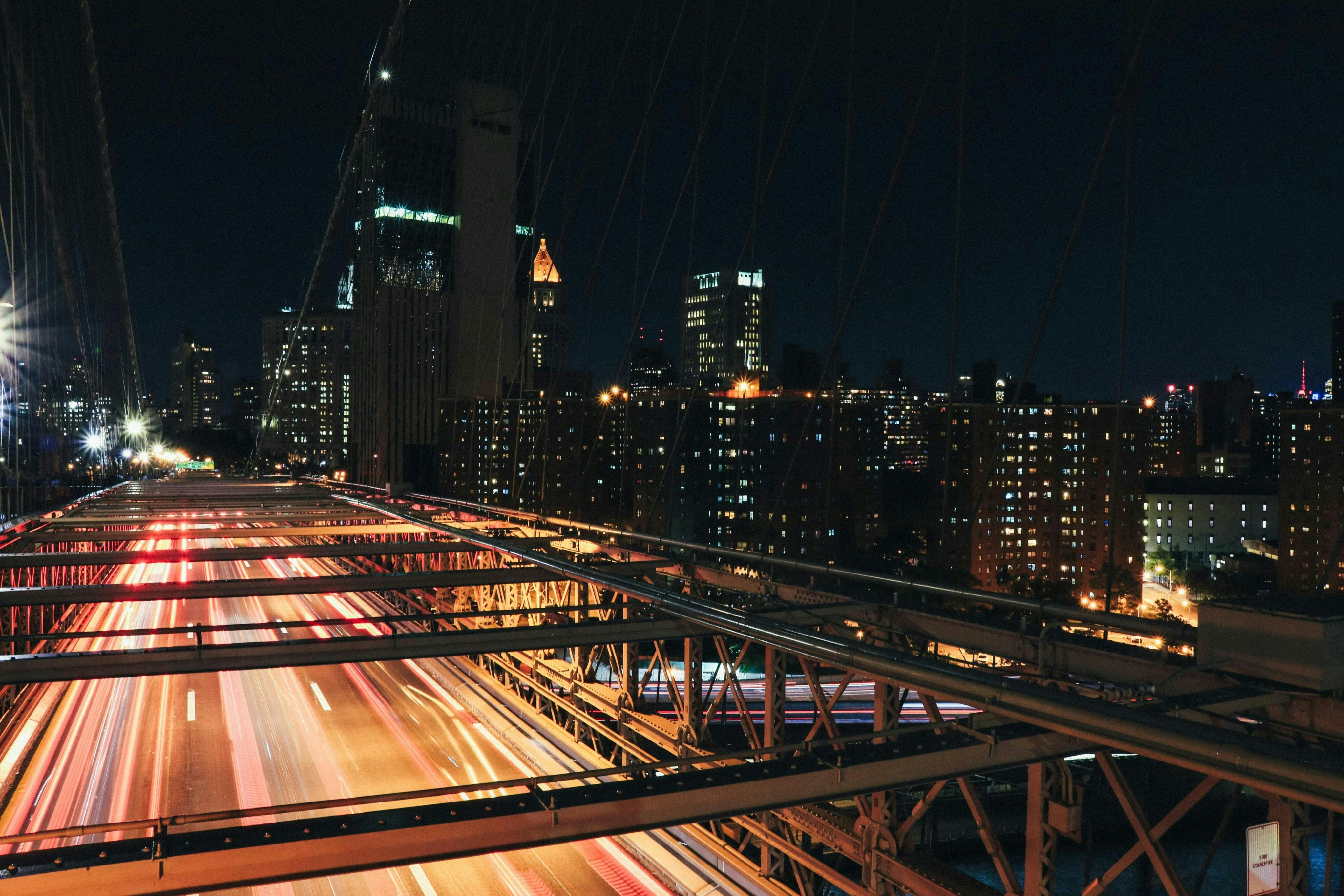 <p>A busy New York City street at dusk, filled with cars and pedestrians. Tall buildings line the road, and streetlights cast a warm glow over the urban scene.</p>
